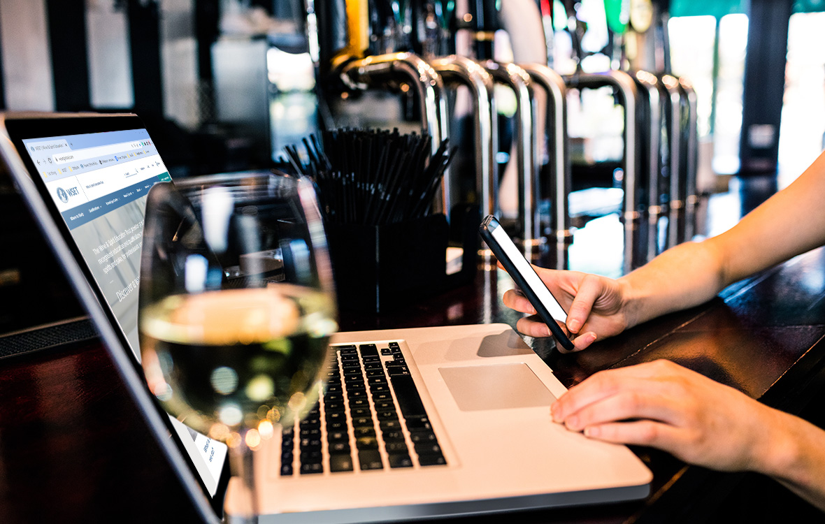 Sitting at a bar with a glass of wine and a laptop, studying WSET wine courses online
