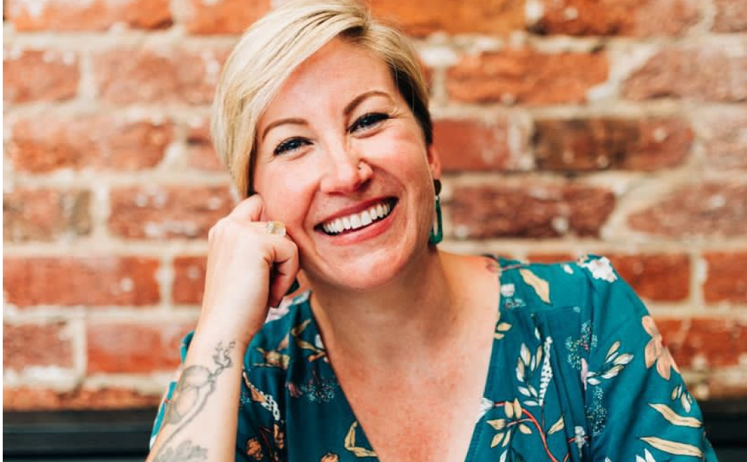 A blonde woman leaning on her arm and smiling