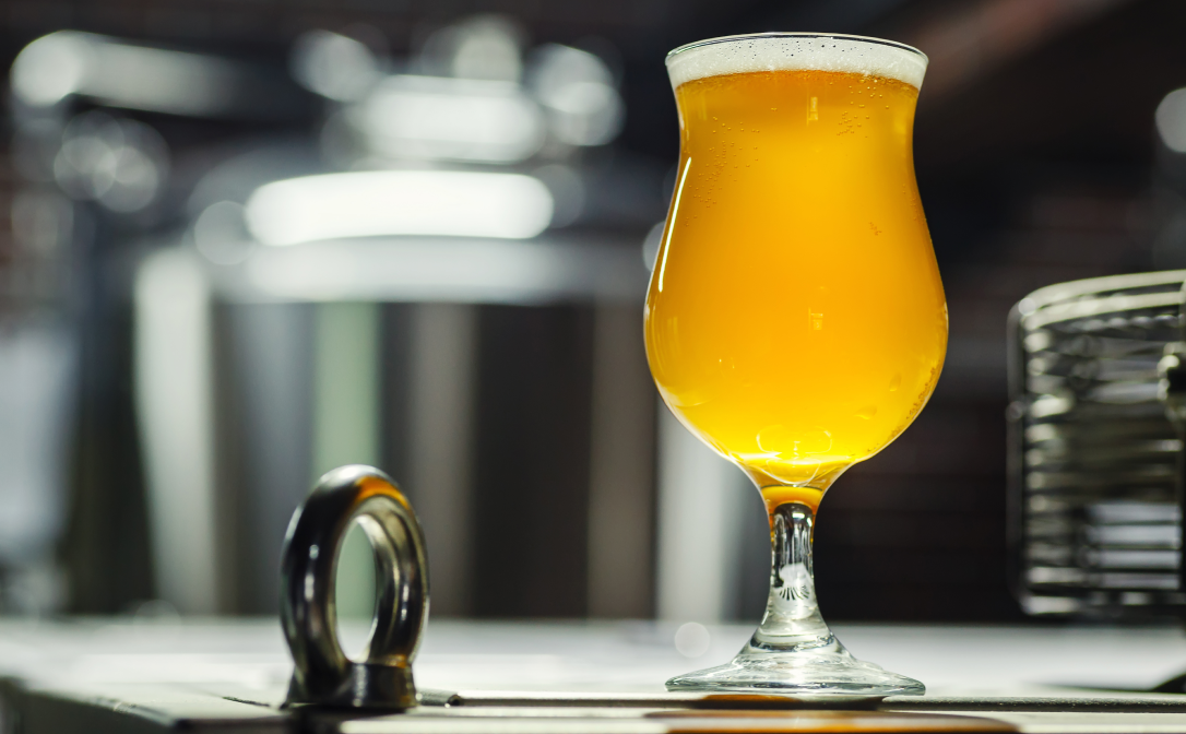 A tulip beer glass, filled with a light beer, in an industrial setting
