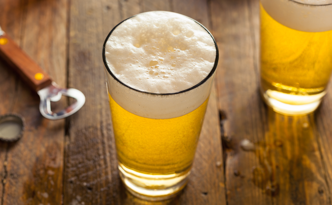 A beer glass with straight sides that get wider towards the top, filled with a light beer
