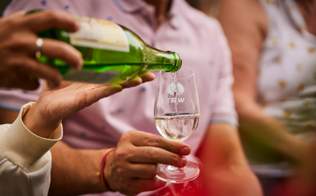 Sake being poured from a green bottle into a small wine glass