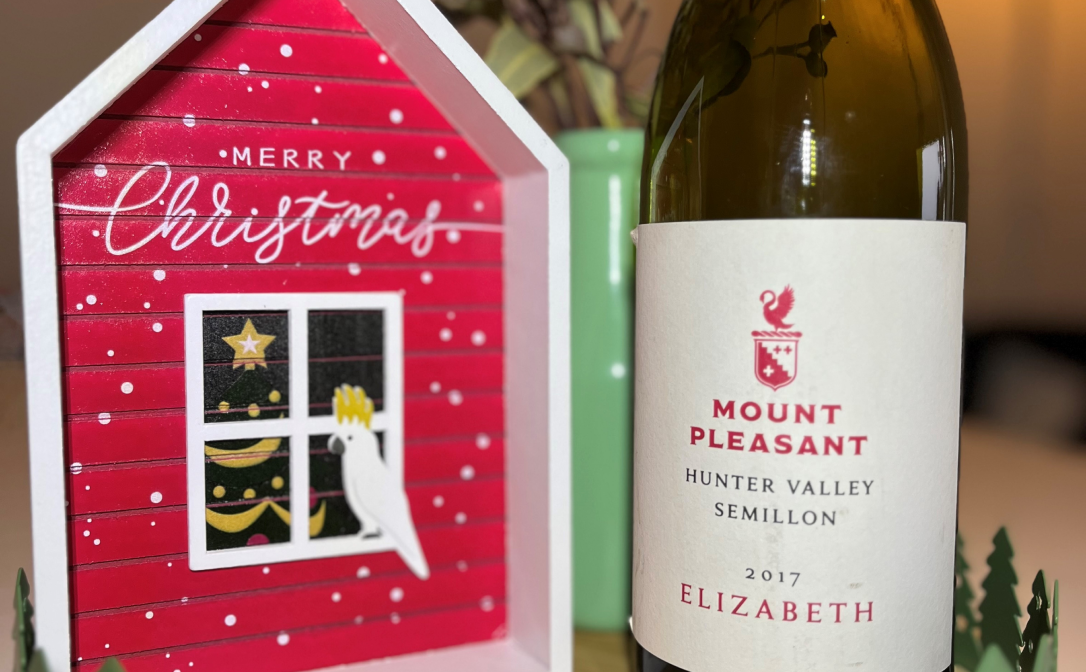 A bottle of wine next to a figurine of a red hut that says Merry Christmas