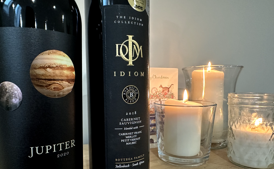 Two bottles of red wine next to white candles and a Christmas card