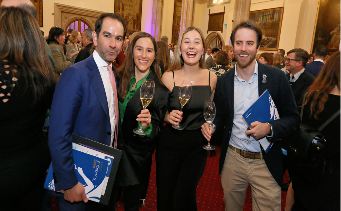 Four people holding glasses of wine and blue yearbooks