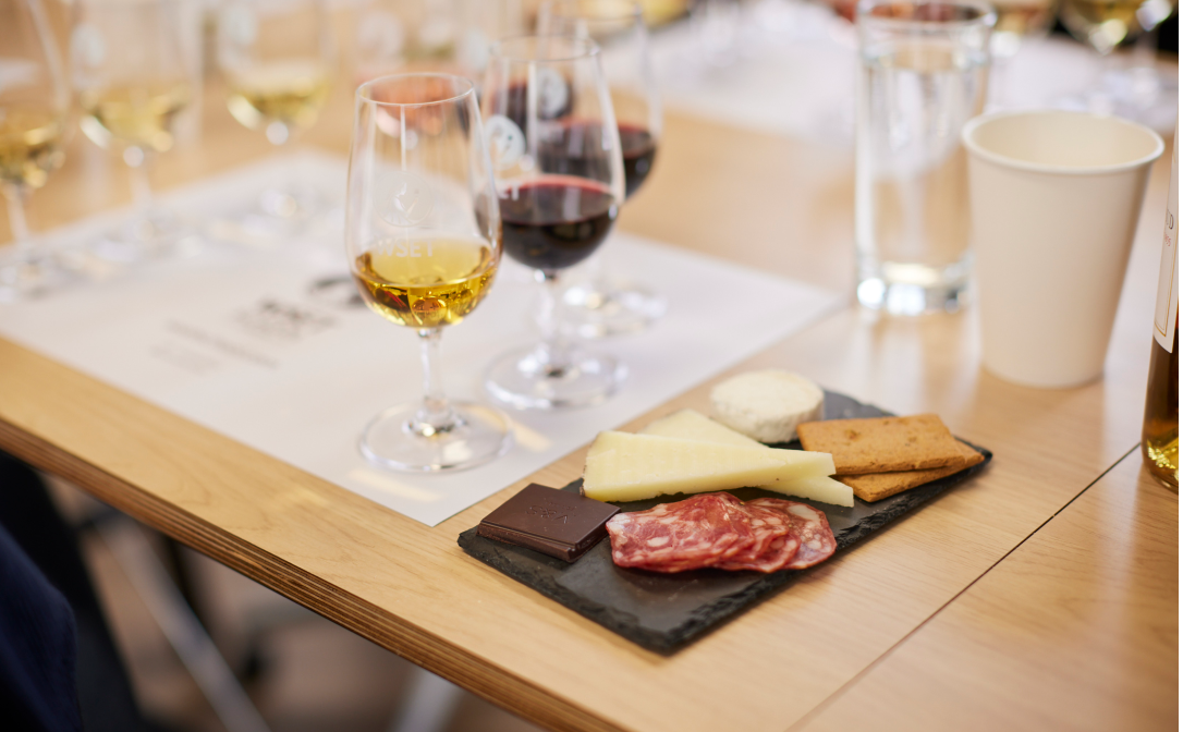 Charcuterie and cheese on a black slate board, with small glasses of wine next to it on a wooden table