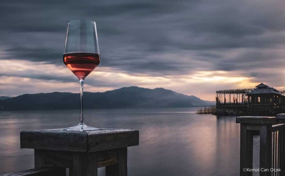 Photograph by Kemal Can Ocak. Red wine on a wooden post, overlooking tranquil waters